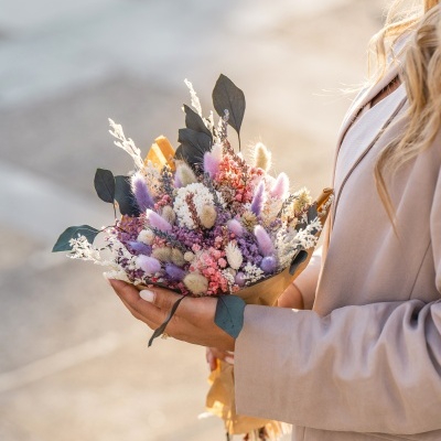 Ramo de flores secas coloridas segurado por mulher com casaco bege