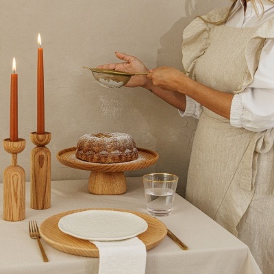 Conjunto de jantar minimalista com pratos brancos, talheres dourados, castiçais de madeira e bolo polvilhado com açúcar em pó em fundo bege