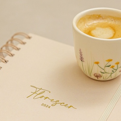 Agenda cozida beige com texto dourado e chávena de café floral