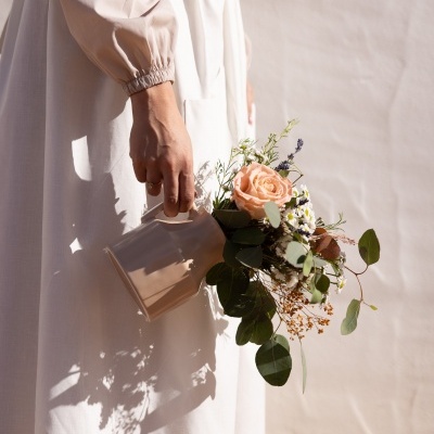 Mulher a segurar jarro cerâmico com flores variadas, vestindo vestido branco de mangas bufantes