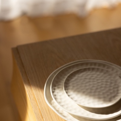 Três pratos de cerâmica branca empilhados sobre mesa de madeira clara