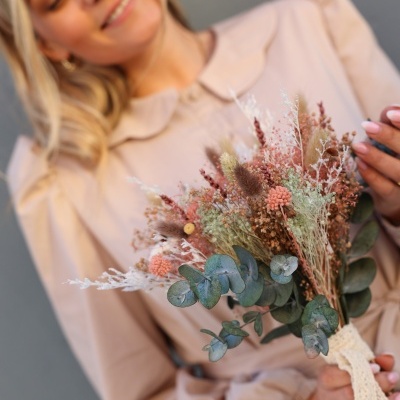 Arranjo de flores secas com fita de renda branca na mão de mulher com blusa creme