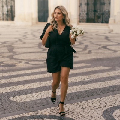 Mulher com macacão preto e sandálias pretas caminhando em calçada de mosaico português