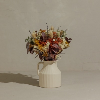 Arranjo floral de flores secas em jarro branco de cerâmica sobre superfície cinzenta