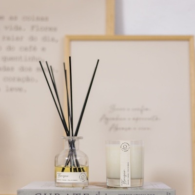 Difusor aromático em frasco de vidro com varetas e vela branca sobre livros decorativos em superfície de madeira