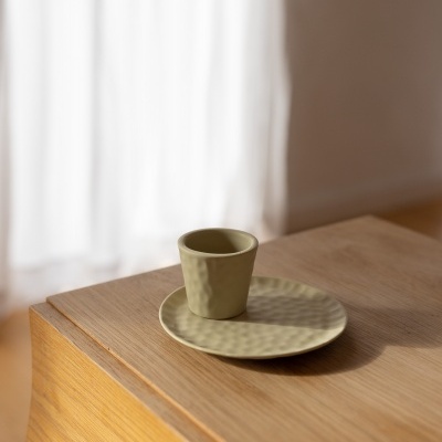 Chávena verde-oliva e pires em cerâmica sobre mesa de madeira clara