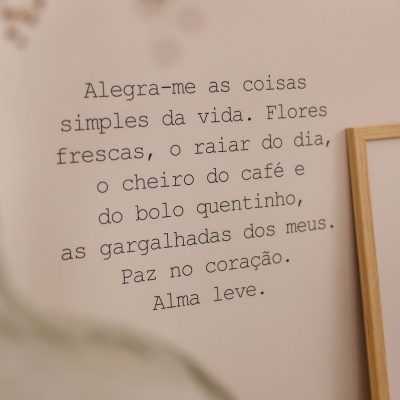 Texto inspirador em parede clara com moldura de madeira e objeto desfocado em vidro