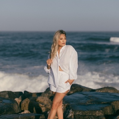 Mulher com camisa branca e calções brancos em rochas na praia