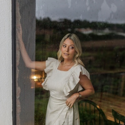 Mulher loira com vestido creme junto a janela com vidro molhado