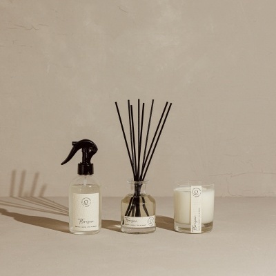 Conjunto de pulverizador, difusor de aroma e vela com embalagens brancas e pretas em fundo bege.