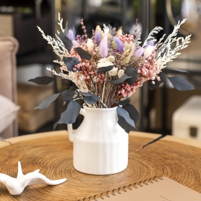 Arranjo floral em vaso branco com flores secas e folhagem sobre mesa de madeira rústica