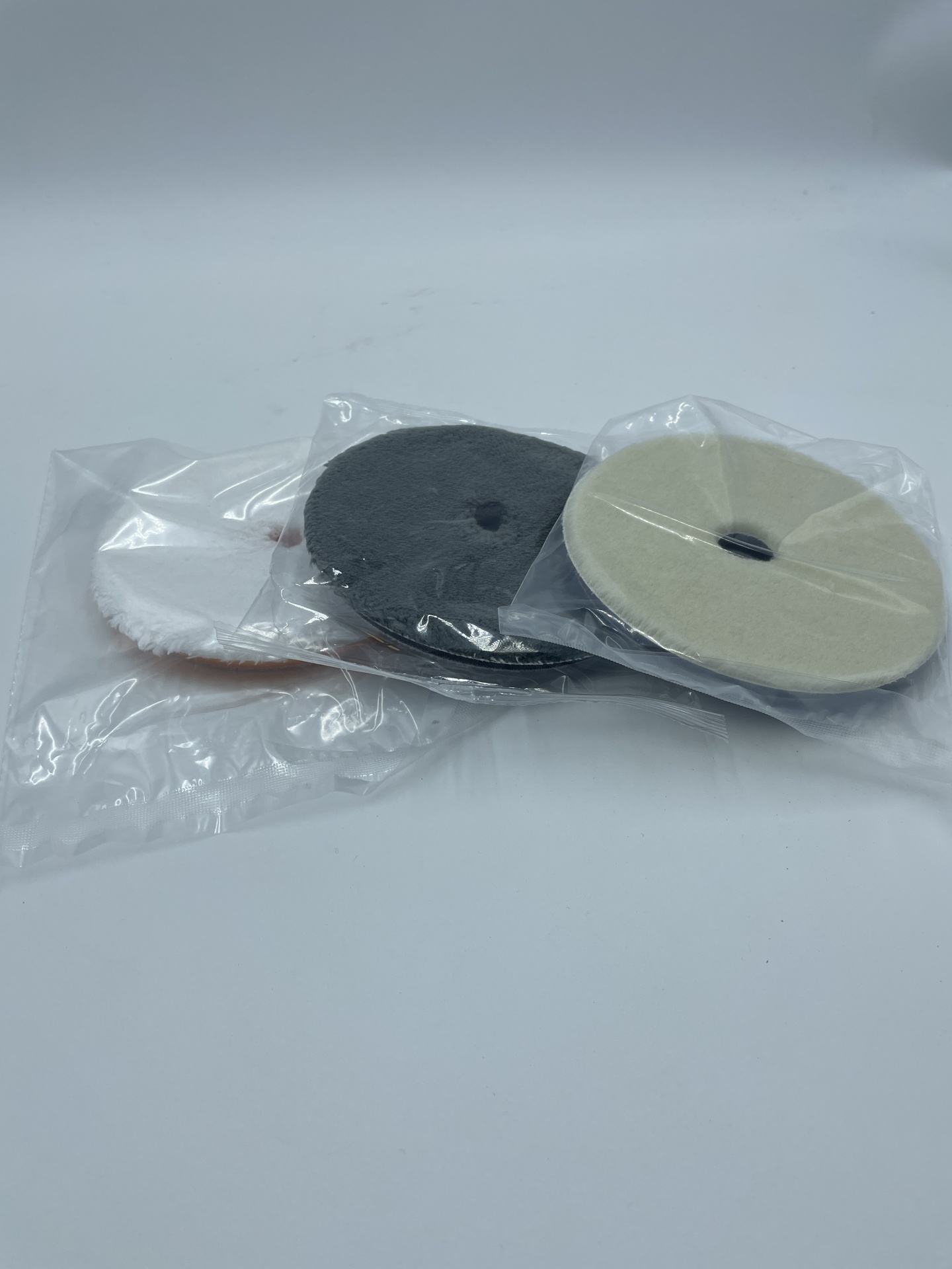 Três discos de polimento embalados em plástico, de cores branco, preto e bege.