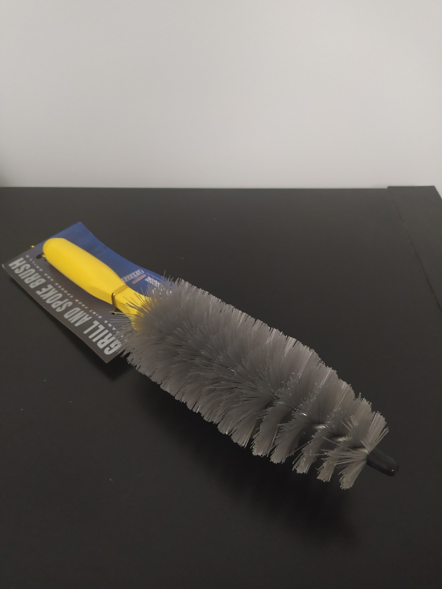 Escova de limpeza com cabo amarelo e cerdas cinzentas sobre superfície preta