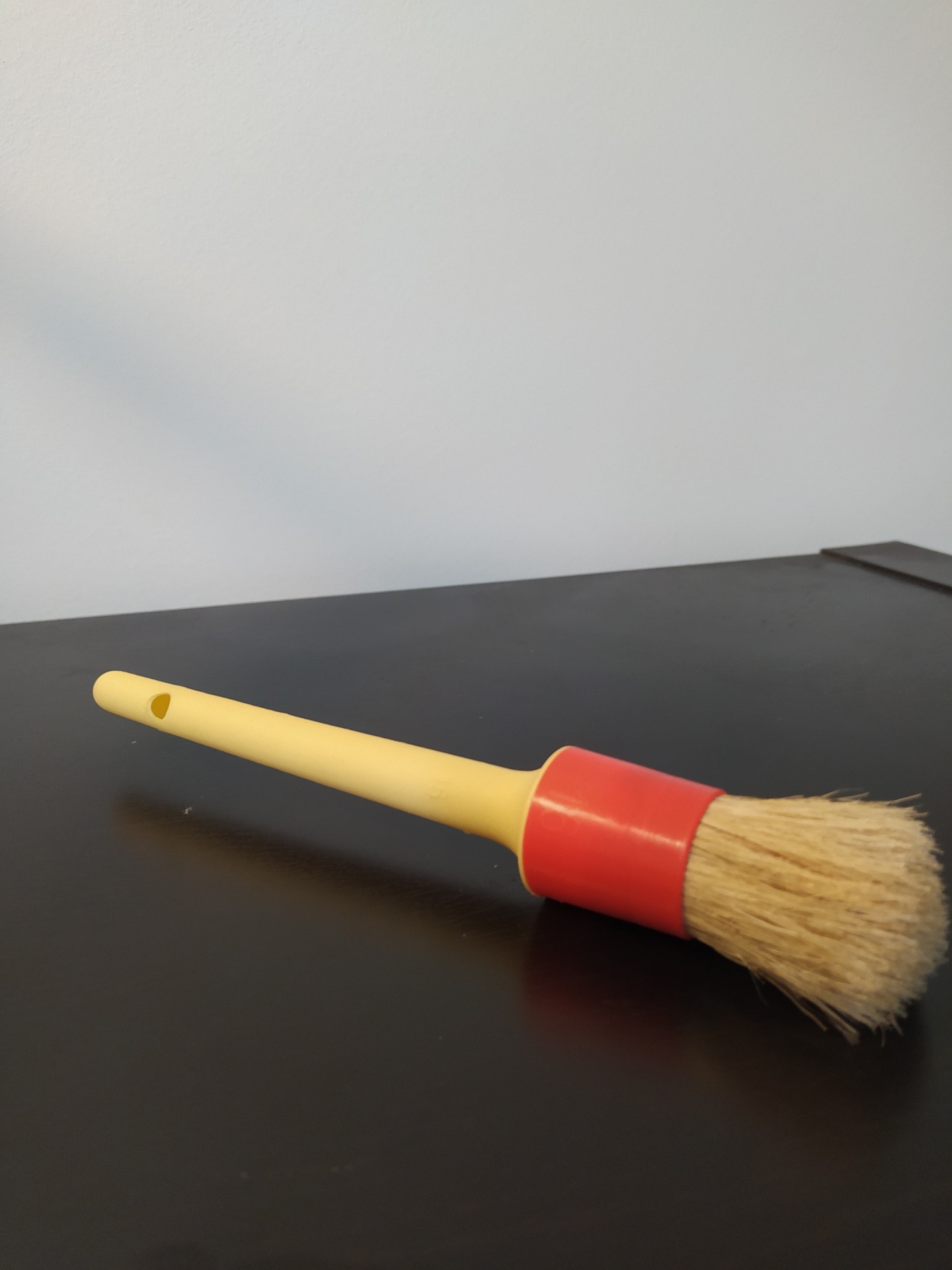 Pincel com cabo amarelo e cerdas naturais com base vermelha em superfície preta