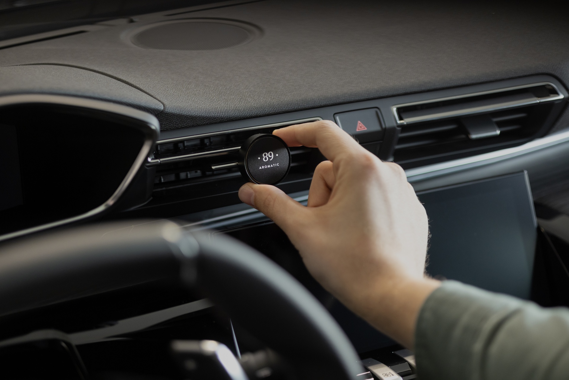 Painel de carro com mão a ajustar dispositivo redondo preto no sistema de ventilação com texto .89 AROMATIC.