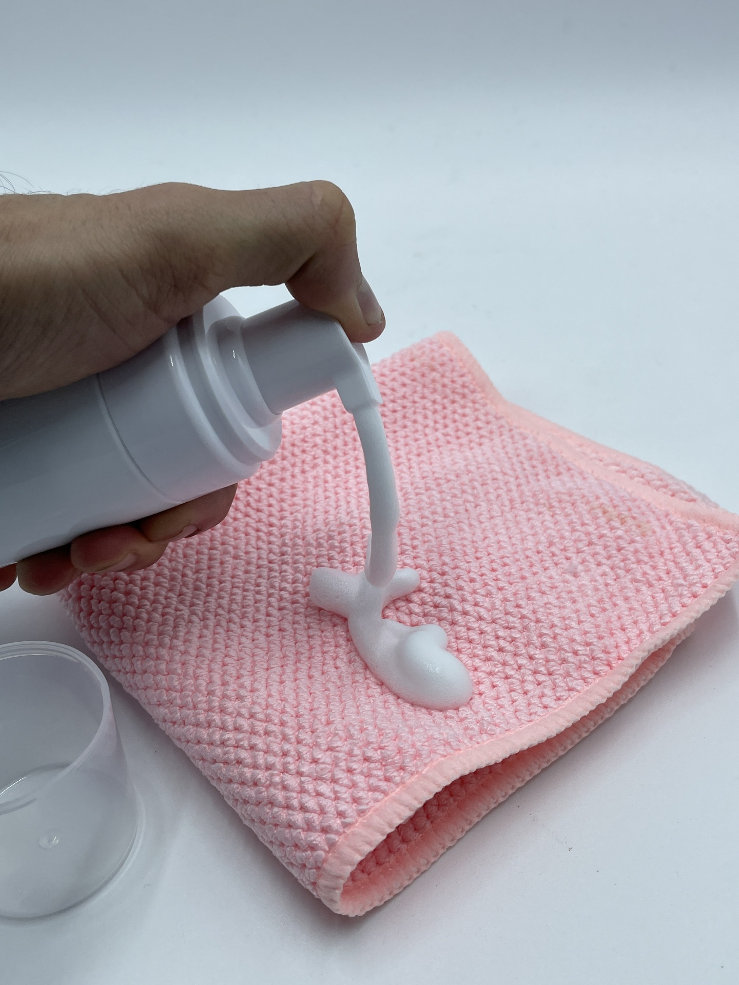 Mão a pressionar dispensador branco a ceder creme sobre pano rosa texturizado