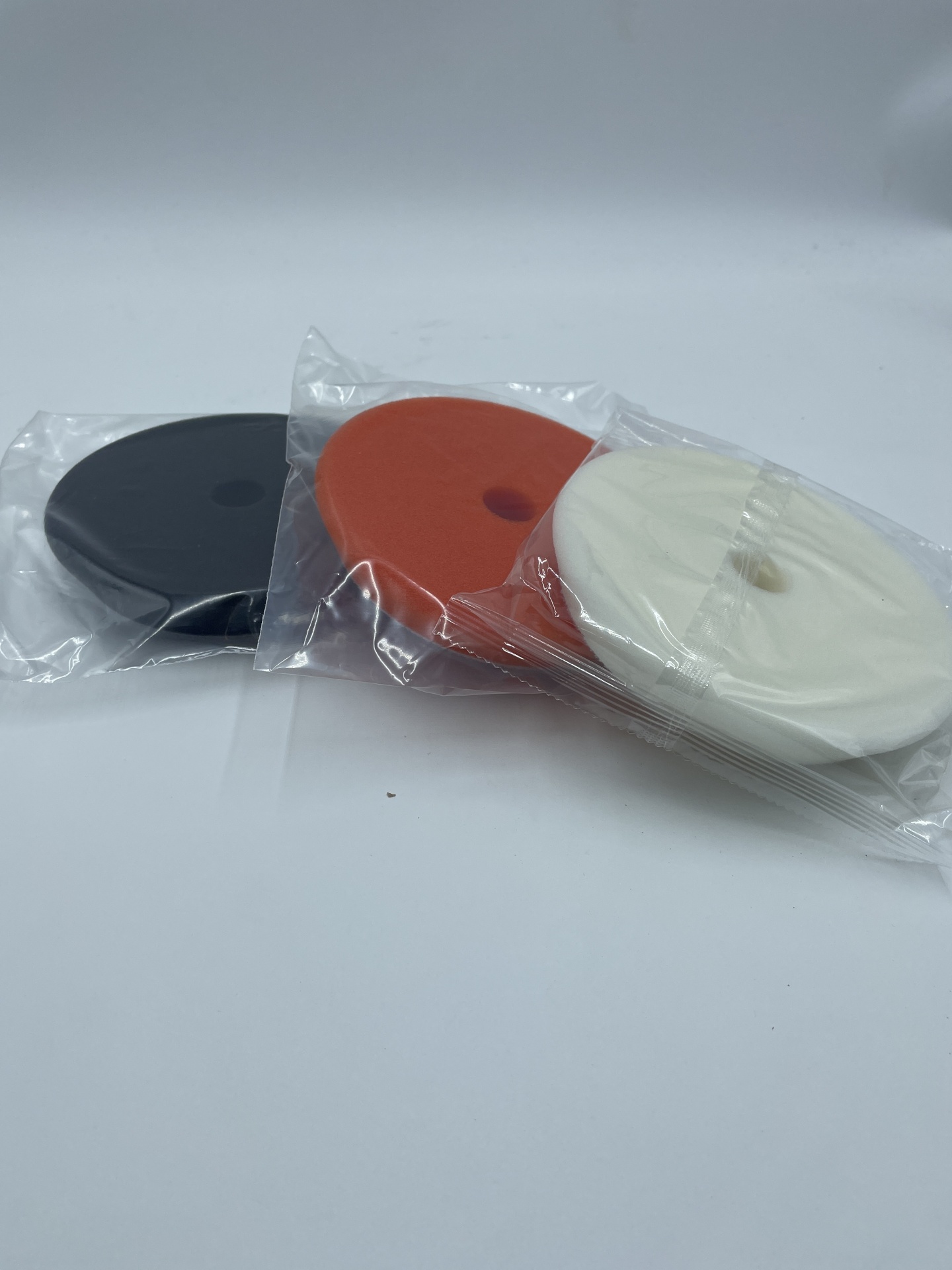 Três esponjas de polimento em plástico transparente de cores preta, laranja e branca