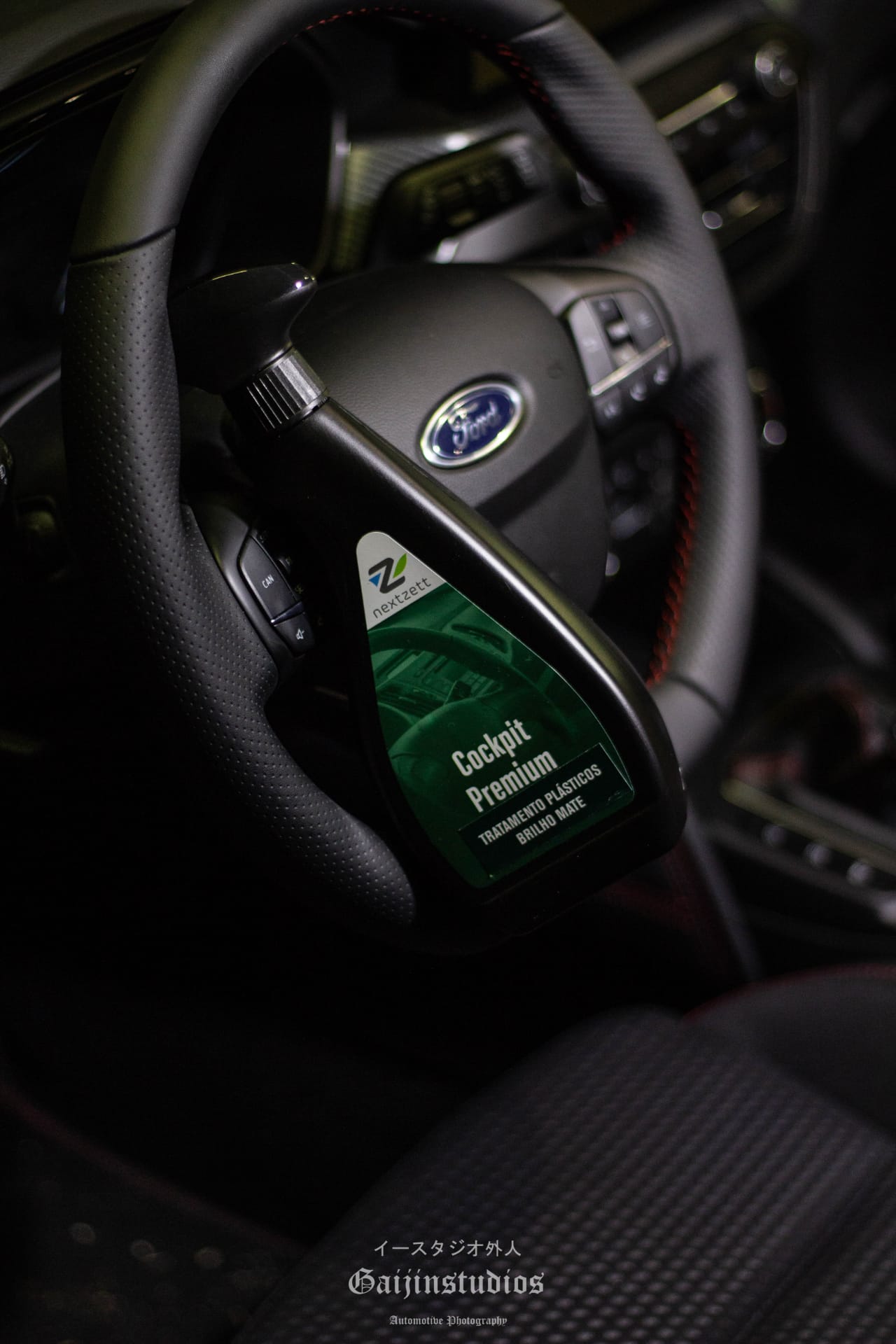 Produto de limpeza para automóveis 'Cockpit Premium' numa embalagem preta com rótulo verde, perto do volante de um carro Ford