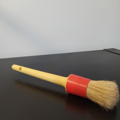 Pincel com cabo amarelo e cerdas naturais com base vermelha em superfície preta