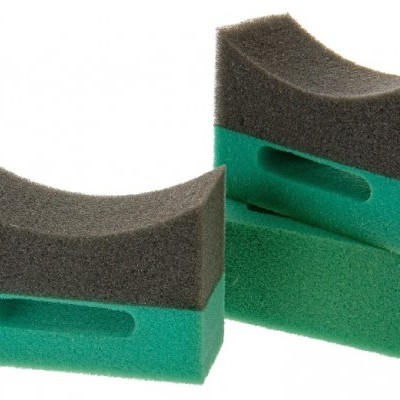 Duas esponjas de limpeza preta e verde com formato curvado e orifício central.