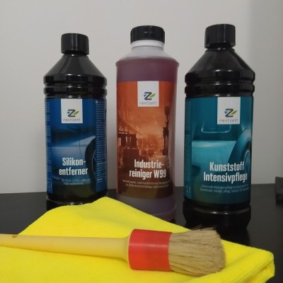 Três frascos de produtos de limpeza nextzett com um pano amarelo e um pincel em superfície preta
