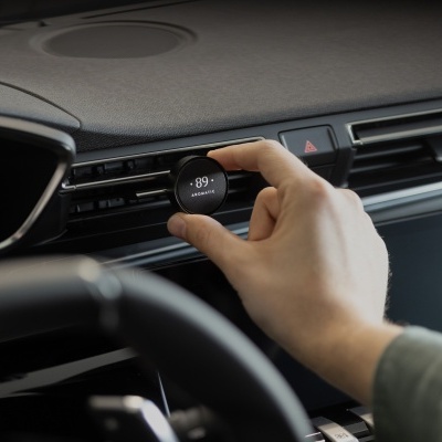 Painel de carro com mão a ajustar dispositivo redondo preto no sistema de ventilação com texto .89 AROMATIC.