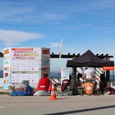 Estande ao ar livre numa estrada com tenda preta, equipamentos e banners coloridos