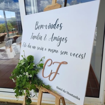 Placa de boas-vindas com texto e decoração floral apoiada em cavalete de madeira
