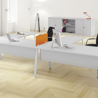 Mesa dupla branca de escritório com cadeiras pretas e móveis cinzentos em espaço com chão de madeira clara