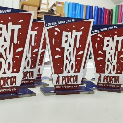 Troféus vermelhos com texto branco sobre mesa branca e fundos de vinis coloridos.