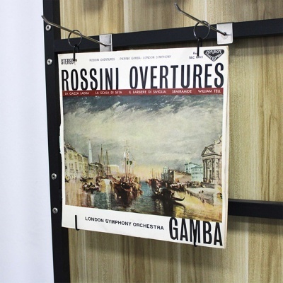 Capa de disco de vinil com título 'ROSSINI OVERTURES' pendurada numa moldura preta em painel de madeira clara