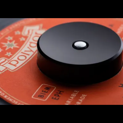 Adaptador giratório preto sobre disco de vinil com rótulo laranja e texto branco.