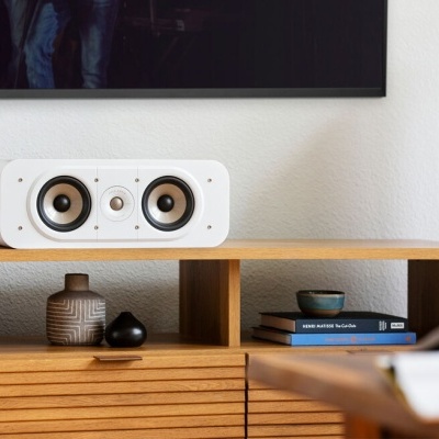 Coluna de som branca com duas colunas laterais pretas sobre móvel de madeira com decoração