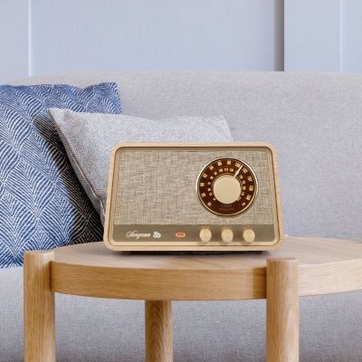 Rádio retro em madeira clara sobre mesa de madeira, com sofá e almofadas ao fundo