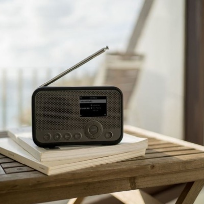 Rádio portátil preto com antena sobre almofadas numa mesa de madeira