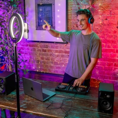 Jovem a fazer DJ em ambiente interior com mesa de madeira, controlador DJ, laptop e anel de luz LED