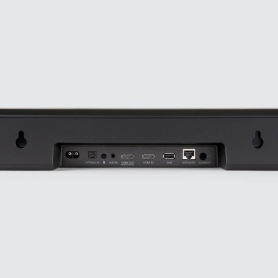 Barra de som preta com várias portas na parte traseira, sobre fundo cinzento