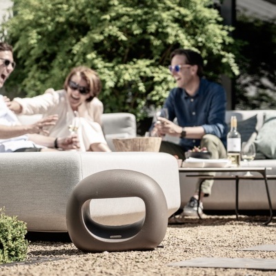 Caixa de som portátil cinza escuro ao ar livre junto a sofá cinza