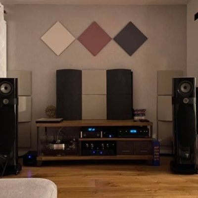 Sistema de áudio com colunas de chão pretas e mesa de som em madeira numa sala com decoração minimalista