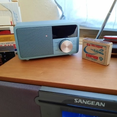 Rádio portátil azul claro numa mesa com caixa de fósforos e objetos de escritório