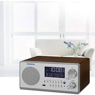 Rádio portátil Sangean com painel frontal prateado e ecrã LED azul em sofá branco