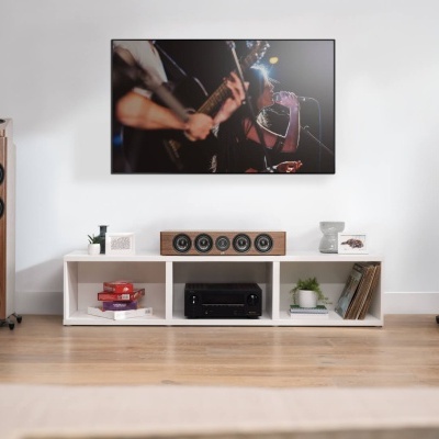 Sistema de entretenimento doméstico com colunas de madeira, coluna central, televisão na parede e estante branca com objetos