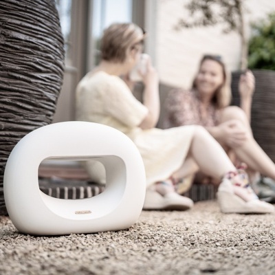 Lâmpada portátil branca em chão de pedra entre vasos escuros grandes e duas pessoas ao fundo.