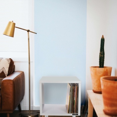 Mesa de apoio branca com discos vinil, cadeira de couro castanho, lâmpada dourada e vasos com plantas