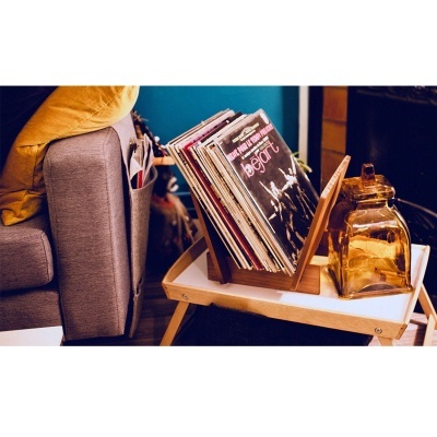 Suporte de discos em madeira com vários discos de vinil perto de um sofá e recipiente de vidro âmbar