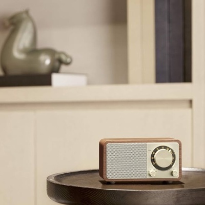 Rádio retro em madeira clara sobre mesa preta com estante branca ao fundo