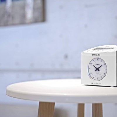 Relógio analógico branco SANGEAN numa mesa redonda branca com pés de madeira
