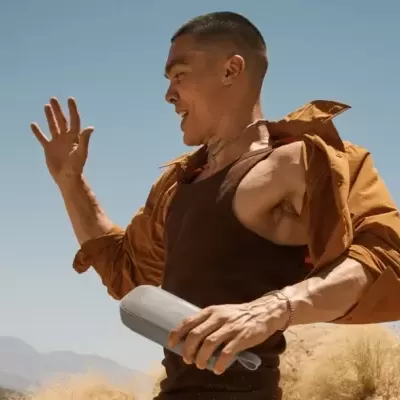 Homem segurando garrafa térmica cinza em área desértica com céu azul