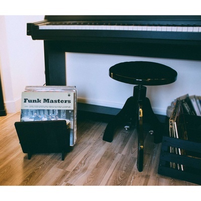 Piano preto com banco, suporte de discos de vinil e capa 'Funk Masters' no chão de madeira.
