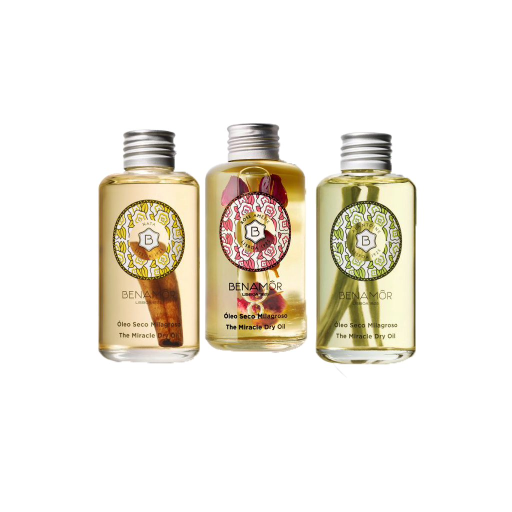 Benamôr - Óleo Seco Três frascos transparentes de óleo seco para corpo BENAMÔR com rótulos coloridos e tampas prateadas